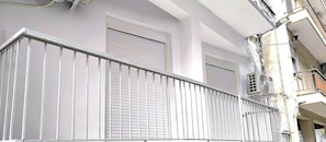 Ein Balkon mit Metallgeländern, ein geschlossenes Fenster mit Rollläden und eine Klimaanlage an der Wand.