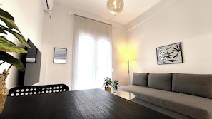 Ein modernes Zimmer mit einer Couch, einem Esstisch, einer Lampe und einer Pflanze.