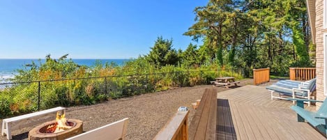 En terrasse med bålsted, liggestole og udsigt over havet.