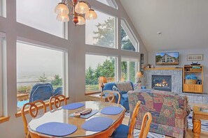 Un comedor con mesa y sillas, chimenea y ventanas amplias.