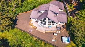Oversigtsbillede af et hus med stor terrasse, jacuzzi og en indhegnet have omgivet af tæt skov.