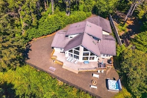 Vista aérea de una casa con un amplio balcón, jacuzzi y jardín vallado rodeado de bosque denso.