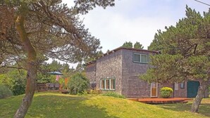 Una casa de dos pisos con fachada de ladrillo, un porche delantero y un pequeño jardín frontal con árboles.