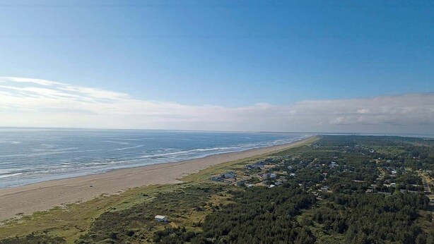 Paisaje costero con playa, zona boscosa y un pequeño asentamiento.