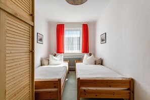 Ein Zimmer mit zwei Holzbett, einer Heizung und einem Fenster mit roten Vorhängen.