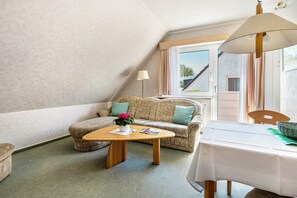 Een kamer met een bank, een tafeltje, een lamp, een raam en uitzicht op buiten.