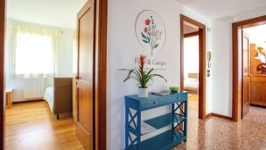 A hotel room with a wooden floor, a bed, a blue console table with a potted plant, and a wall with a floral design.