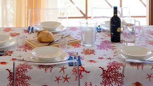 A dining table set with plates, glasses, a bottle, and a lamp, with a view of trees through a window.