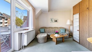 Ein modernes Wohnzimmer mit Sofa, Hocker und Couchtisch, einem Heizkörper, einem Fenster mit Blick auf Gebäude und einem Holzschrank.