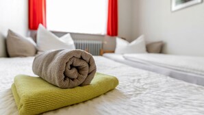 Ein ordentlich bezogenes Bett mit einem aufgerollten und einem gefalteten Handtuch auf einer weißen Bettdecke.