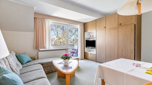 Ein modernes Wohnzimmer mit einer Couch, einem Couchtisch mit Blumenvase, einem Fernseher und einem Essbereich mit Tisch.