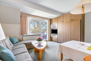 Ein modernes Wohnzimmer mit einer Couch, einem Couchtisch mit Blumenvase, einem Fernseher und einem Essbereich mit Tisch.