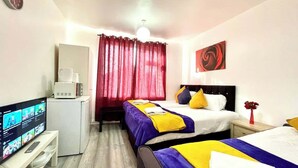 Ein Hotelzimmer mit zwei Betten, einem Fernseher, einer Minikühlschrank und einem roten Vorhang.