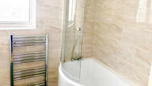 Ein Badezimmer mit einer gläsernen Duschkabine, einer weißen Badewanne und einem chromfarbenen Handtuchhalter.