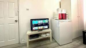 Ein kleiner Raum mit einem Fernseher auf einem Schrank, einem weißen Korpus und einer Uhr an der Wand.