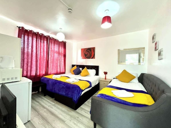 Hotellihuone, jossa on kaksi sänkyä, työpöytä, tuoli, peili ja punainen verho.