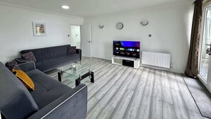 A modern living room with a sofa, TV, glass coffee table, and a white radiator. - Riverview Stunning Apartment 3Bedroom 2Bathroom (Greater London)