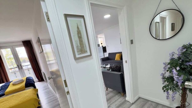 A hotel room with a bed, a desk, a chair, a potted plant, and a mirror on the wall. - Riverview Stunning Apartment 3Bedroom 2Bathroom (Greater London)