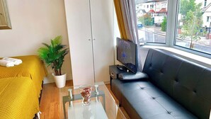 Una stanza con un divano, una TV, un tavolino in vetro, una pianta e un letto con biancheria gialla.
