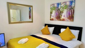 Una cama con ropa de cama amarilla, dos almohadas y un cuadro de un bosque.