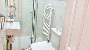Un baño con cabina de ducha de vidrio, un lavabo blanco, un inodoro y un perchero para toallas.