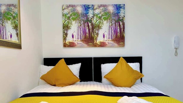 Una habitación de hotel con cama, dos almohadas, una colcha amarilla y dos toallas.