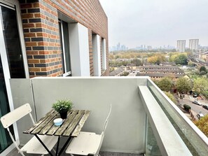 Un balcon avec une table et des chaises, un pot de fleurs et une vue sur le paysage urbain.