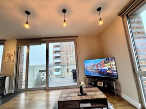 Ein modernes Wohnzimmer mit einem großen Fernseher, einem Holztisch und einer Glastür, die auf einen Balkon führt.
