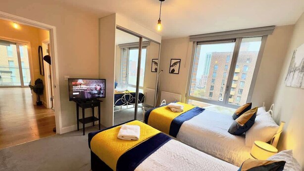 Hotellihuone, jossa on kaksi sänkyä, televisio, työpöytä ja näkymä rakennuksiin.