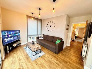 A modern living room with a flat-screen TV, a brown sofa, a wooden coffee table, and a wall clock.