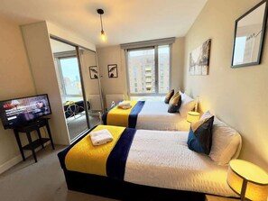 A hotel room with two beds, a TV, and a view of buildings.