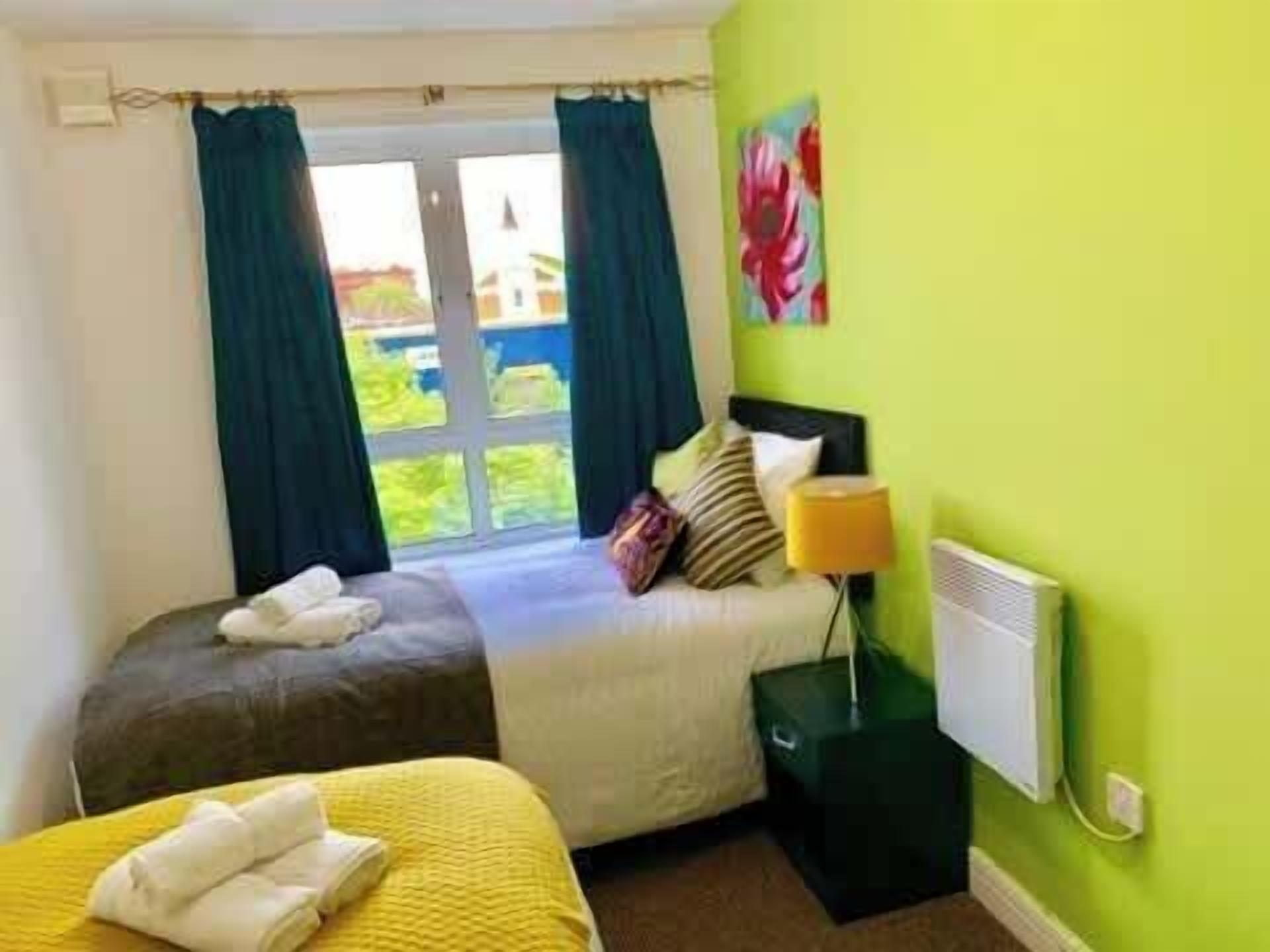 A room with two beds, a window with curtains, a radiator, and a painting on the wall.
