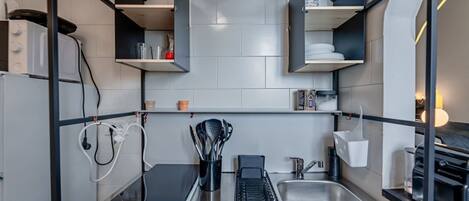 A modern kitchen with a built-in stove, a sink, and a countertop with a coffee machine and utensils.