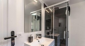 Un bany modern amb plat de dutxa inclòs en vidre, un rentapeus blanc i un mirall gran.