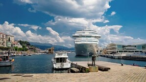 A cruise ship docked at a port with a statue and buildings in the background. - [Historic Palace Duplex] Cruise 2 min • A/C • WiFi (Savona)