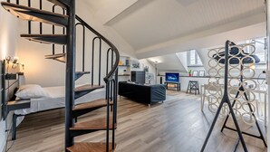A modern loft-style room with a spiral staircase, a bed, a desk, and a TV. - [Historic Palace Duplex] Cruise 2 min • A/C • WiFi (Savona)