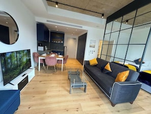 A modern living room with a TV, sofa, coffee table, and dining area. - London Cosy flat Balcony, RiverView, O2, Excel (Greater London)