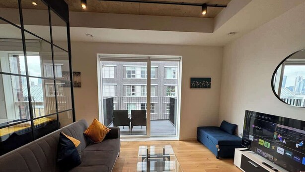 Een moderne woonkamer met een bank, salontafel, televisie en balkon met stoelen.