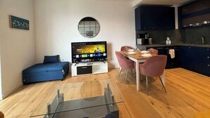 Een moderne woonruimte met een bank, televisie, eettafel, stoelen en een keukenhoek.