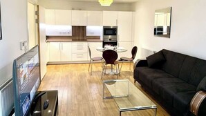 Ein modernes Wohnzimmer mit einem schwarzen Sofa, einem Glastisch und einem Fernseher auf einem Schrank.