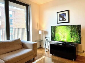 Ein modernes Wohnzimmer mit großem Flachbildfernseher, einer Couch, einem Glastisch und einem gerahmten Bild an der Wand.