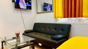 A modern room with a black leather sofa, a glass coffee table, a TV mounted on the wall, and a window with yellow curtains. - Studio flat en-suite, Kitchenette, Parking, NP4 (Newbury Park)