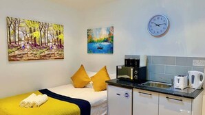 A compact room with a bed, a small kitchenette, a clock, and two paintings on the wall. - Studio flat en-suite, Kitchenette, Parking, NP4 (Newbury Park)