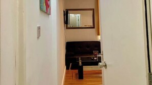 A hallway with a wooden floor, a black sofa, a mirror, and a ceiling light fixture. - Studio flat en-suite, Kitchenette, Parking, NP4 (Newbury Park)