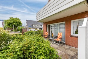 Eine Terrasse mit Tisch und Stühlen, eine Ziegelwand und ein Fenster mit Vorhängen.