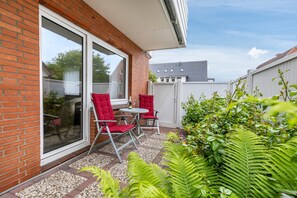 A patio with a brick wall, sliding glass door, red chairs, a small table, and a garden with ferns. - Apartment "No. 10" with Wi-Fi (Büsum)