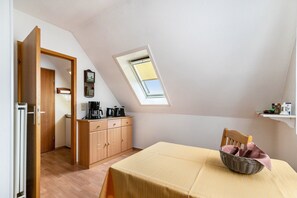 Ein Zimmer mit schrägem Dach, einem Oberlicht, einem Esstisch, einem Holzschrank und einer Küchenzeile.