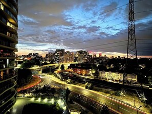 A cityscape at dusk with illuminated buildings, a highway, and a prominent power line tower. - Cosy Apartment, Balcony River View, O2, Cable Car (Greater London)