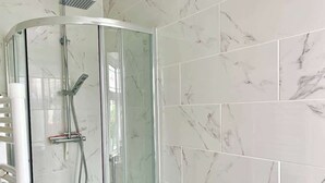 Una ducha con puerta de cristal, un inodoro con papel higiénico y una pared de azulejos blancos.