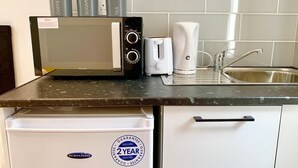 Una kitchenette con microondas, cafetera y tetera sobre la encimera, un fregadero y un refrigerador blanco con etiqueta de garantía de 2 años.